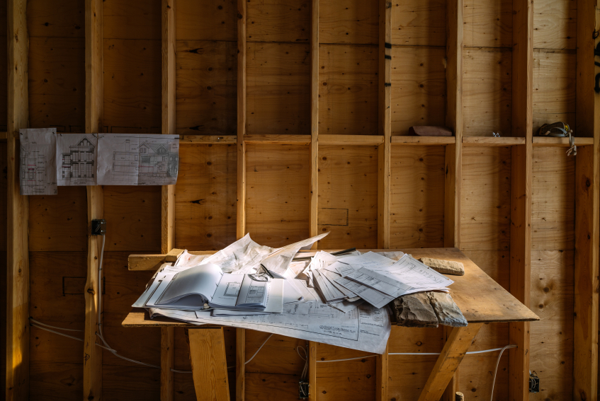 Blue prints and plans for a house on a wooden table in a construction zone