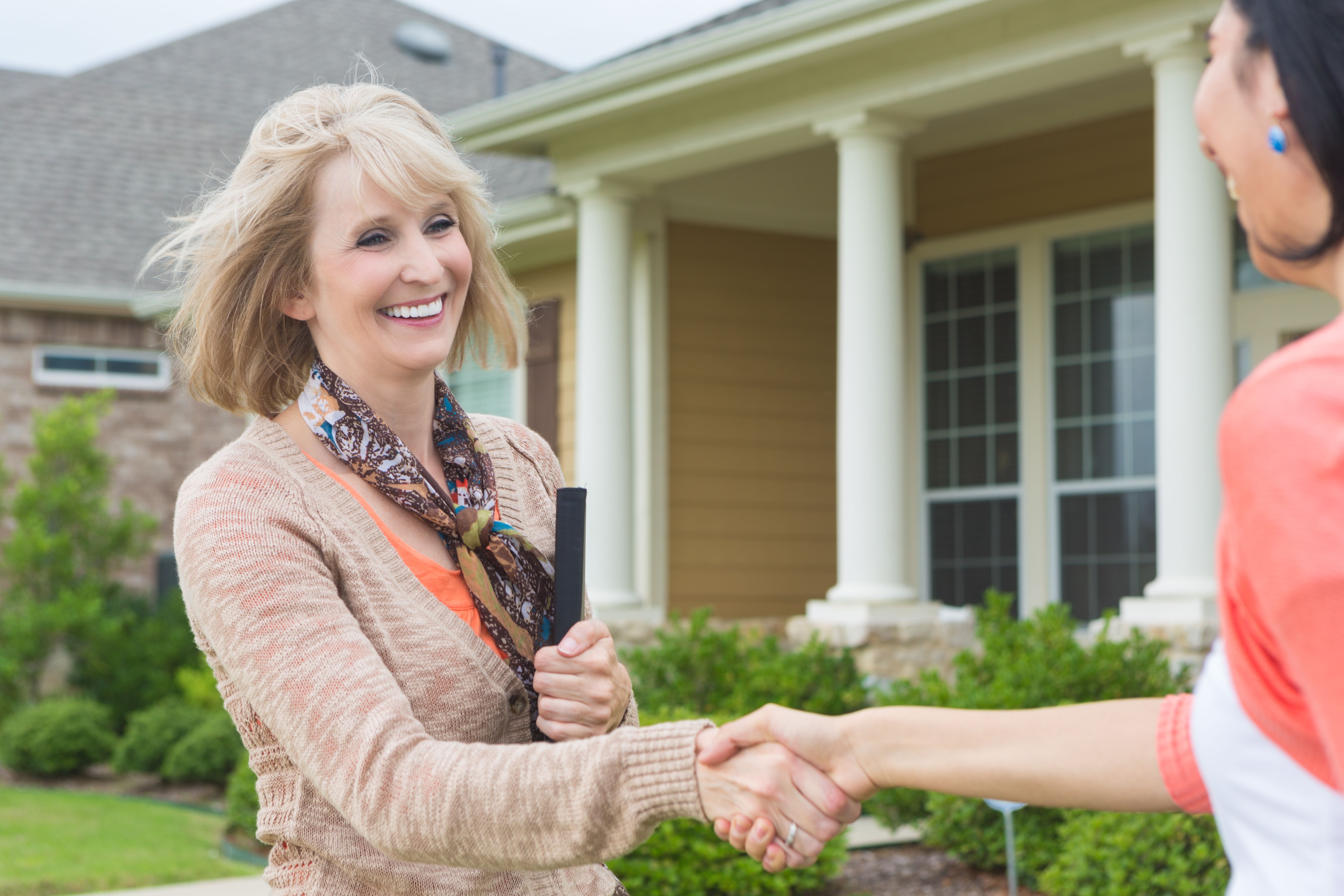 Female Realtor shaking hands with new female homeowner in front of house