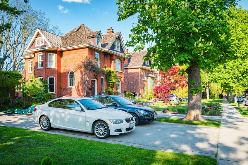2 cars parked in the side driveway of a two story brick house