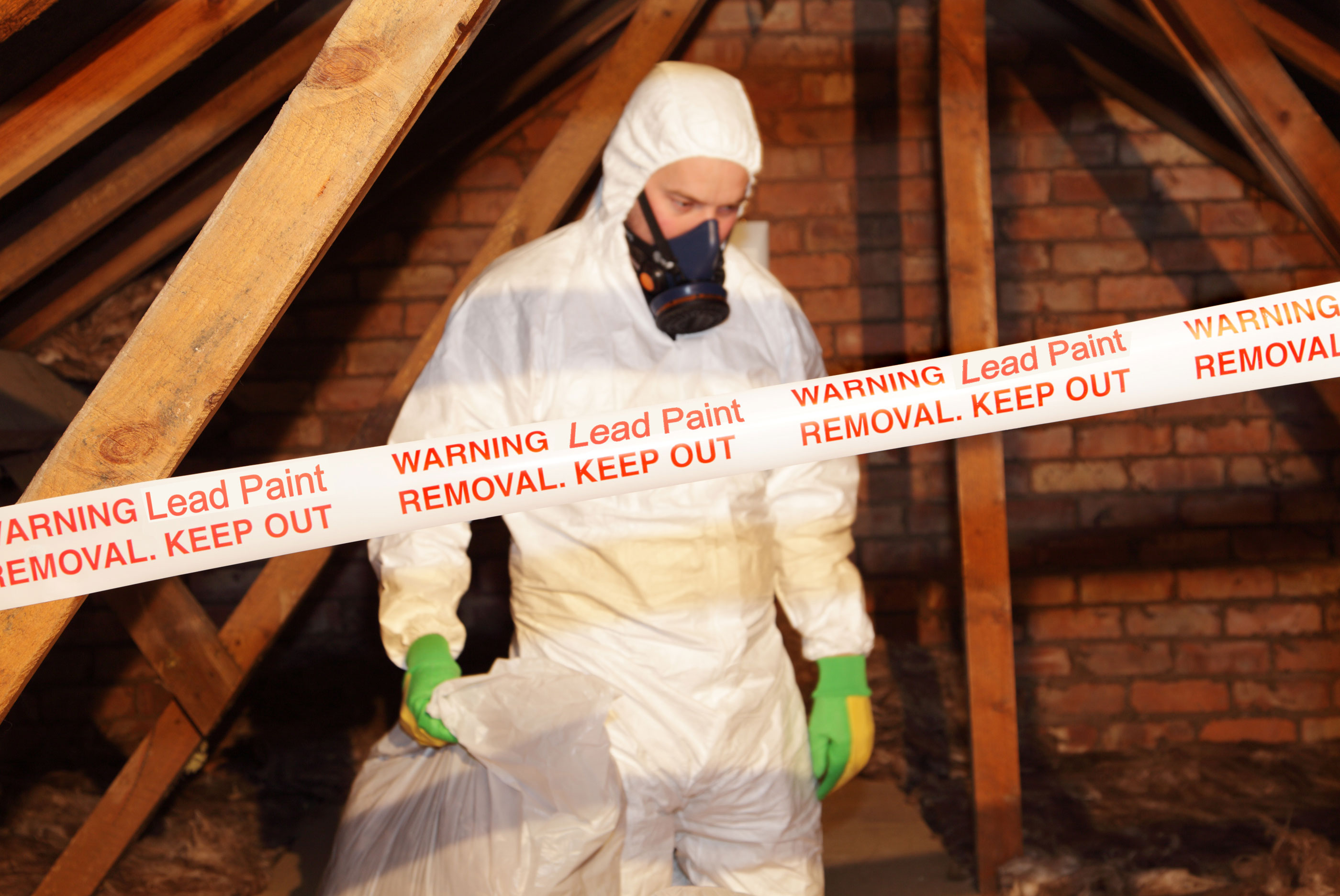 Man in white protective suite and mask in attic moving lead paint